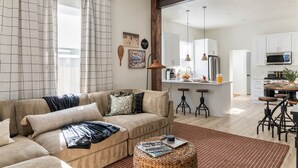 A modern living room with a sofa, coffee table, and a kitchen area with bar stools. - Ski Lodge, Ski Drop, Pickleball, HotTub, Sleeps 12 (South Salt Lake)