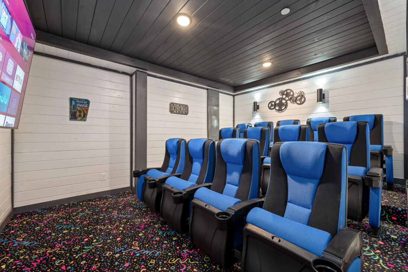 Une salle de cinéma privée avec des fauteuils bleus et noirs, un appareil à pop-corn et un écran mural affichant les différentes options de films.