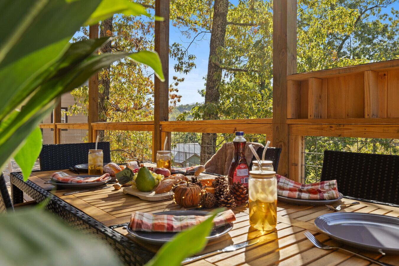 Ein Essbereich im Freien mit einem Holztisch, gedeckt für eine Mahlzeit, umgeben von Bäumen und blauem Himmel.