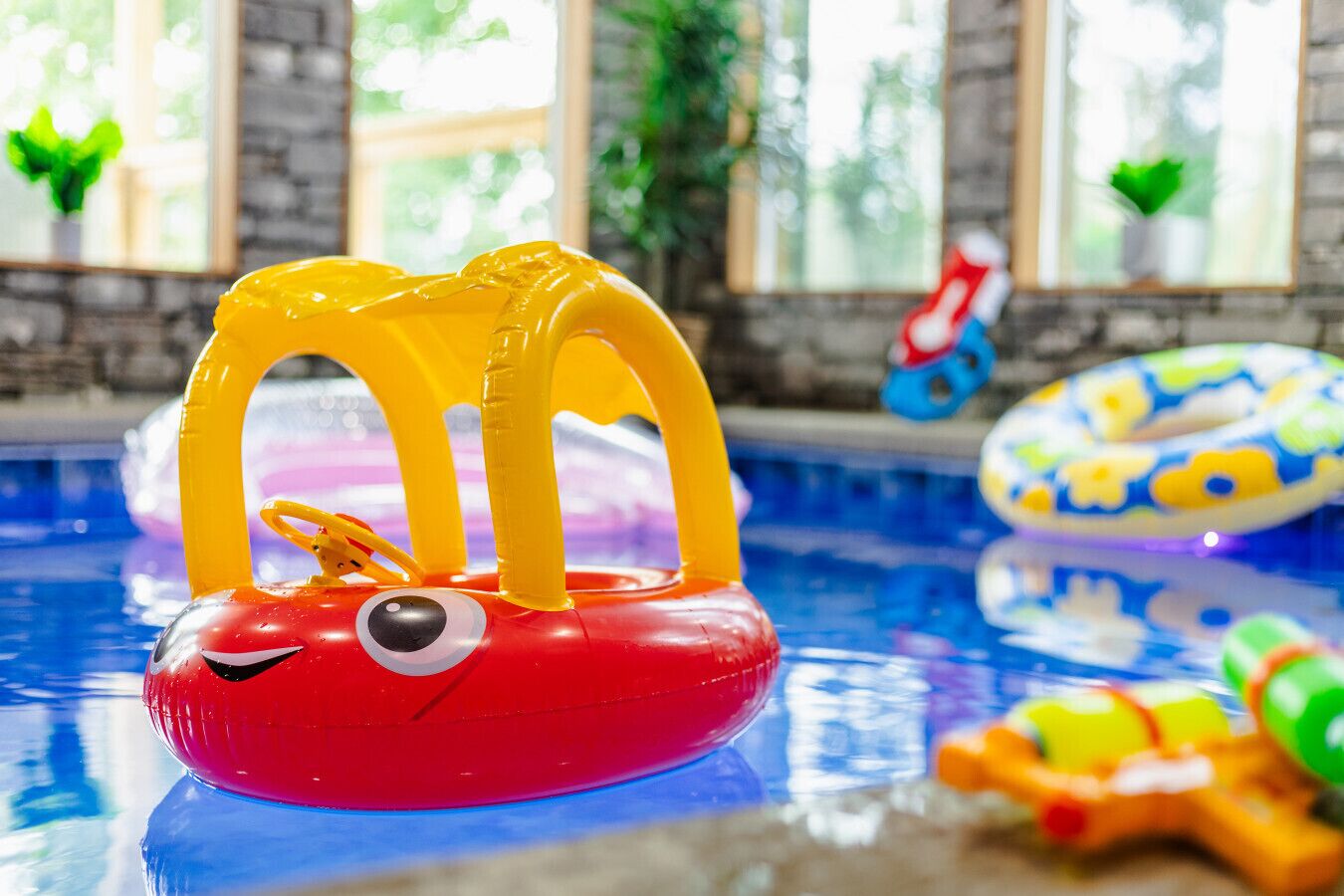 En pool med uppblåsbara leksaker, bland annat en röd krabba med gula bågar och en blå och vit badring formad som en fisk.