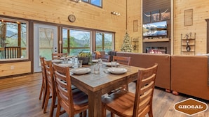 A wooden interior with a dining table set for four, a fireplace, and a Christmas tree. - Summit Luxe Resort (Gatlinburg)