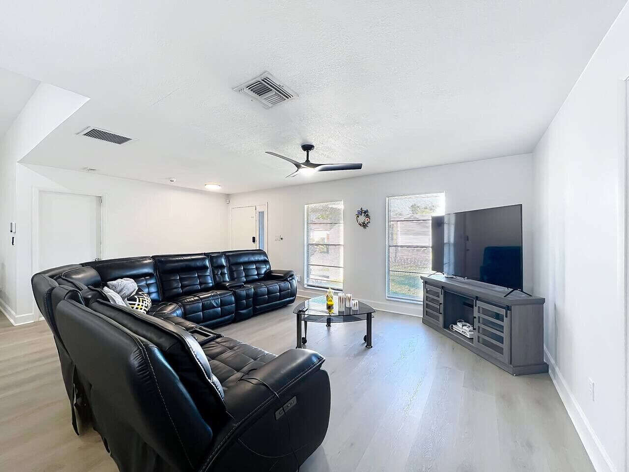 A modern living room with a black leather sectional sofa, a glass coffee table, and a flat-screen TV on a grey entertainment unit.