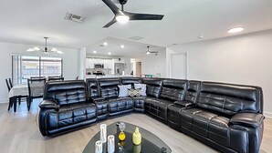 Un salon moderne avec un canapé d’angle en cuir noir, une table basse en verre et un ventilateur de plafond.