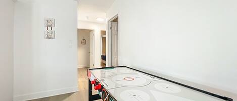 A room with a foosball table, a door, and a hallway leading to another room.