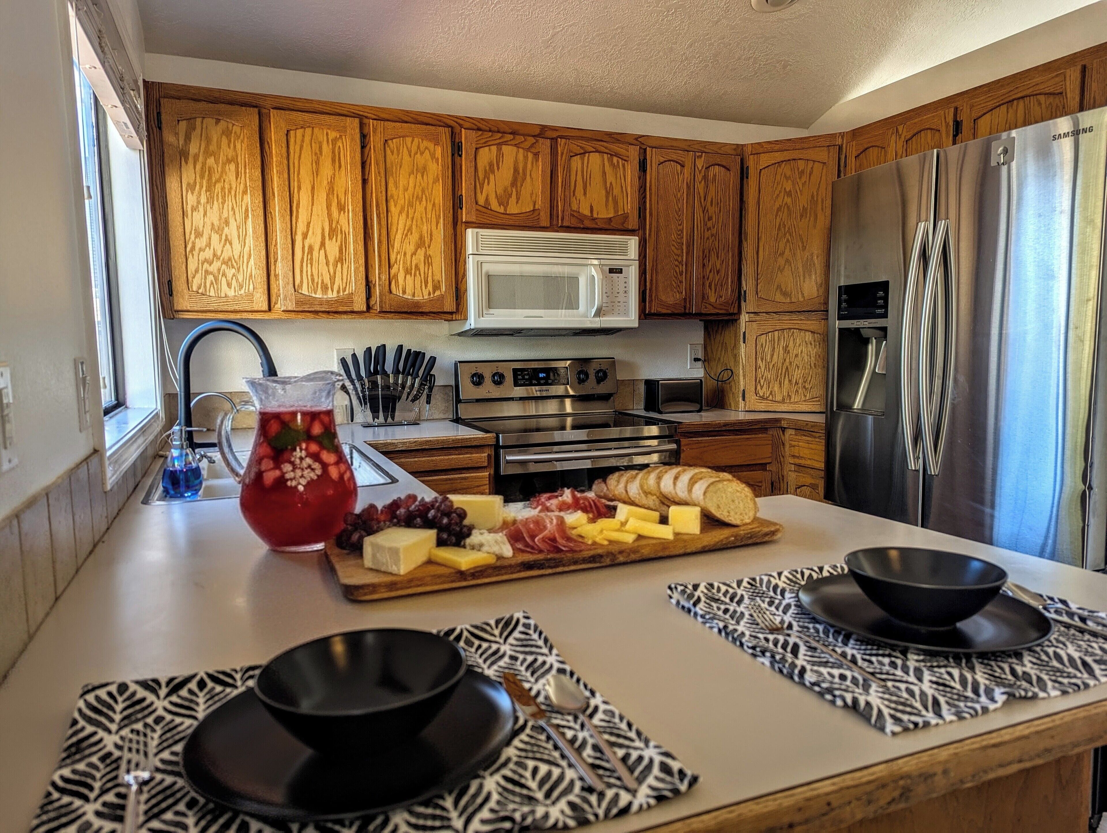 A modern kitchen with wooden cabinets, stainless steel appliances, and a central island with a fruit and cheese board.
