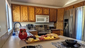 A modern kitchen with wooden cabinets, stainless steel appliances, and a central island with a fruit and cheese board. - 3BR Family Meridian Home ★Sleeps 6 ★ 5 Min to The Village ★ Indoor–Outdoor Patio (Meridian)