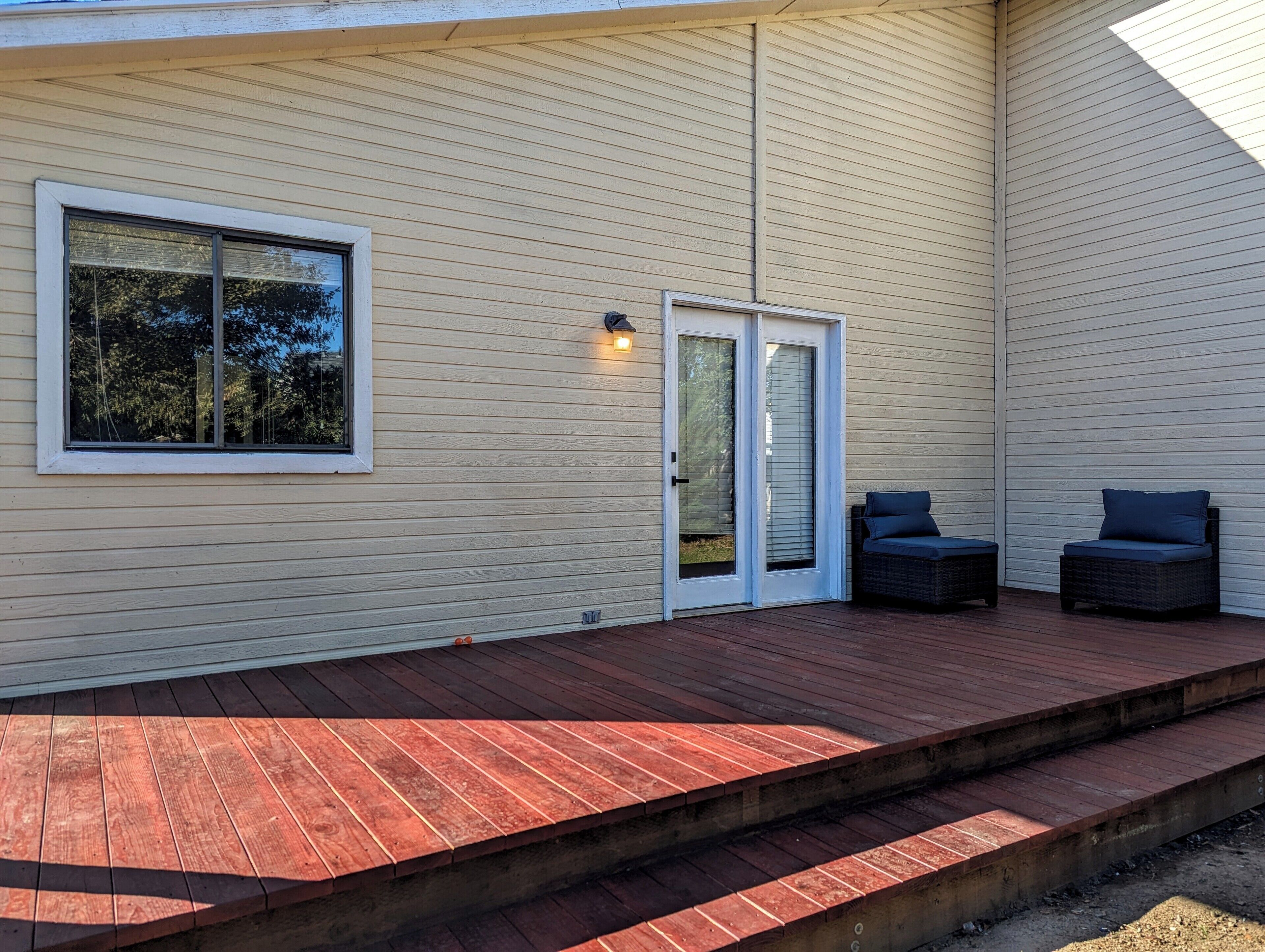 A covered deck with a wooden floor and two dark-colored chairs.