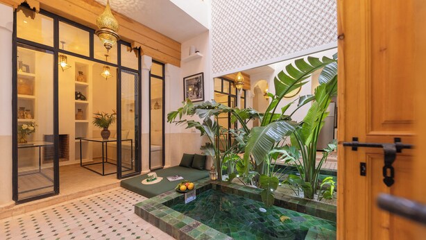 A modern interior with a glass door leading to a balcony, a small seating area with cushions, and a tiled water feature. - Riad Jardin d'Orient - Riad with 2 pools in the heart of the Medina (Marrakech)