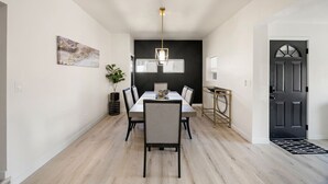 A modern dining area with a long table, chairs, a pendant light, a black-framed mirror, and a black door. - Downtown Ebony- 1.5 Miles from Whiskey Row (Prescott)