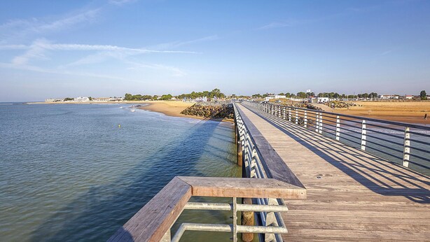 A wooden boardwalk extending into the ocean, with a sandy beach and a clear sky in the background. - Maison au coeur de la vendée (La Jonchere)