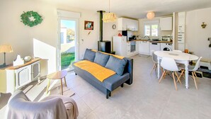 A modern living room with a sofa, a dining table, and a kitchen area. - Maison au coeur de la vendée (La Jonchere)