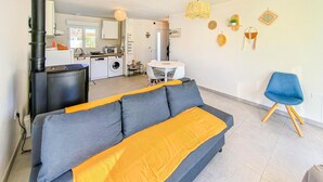 A modern living room with a grey sofa, a blue chair, and a kitchen in the background. - Maison au coeur de la vendée (La Jonchere)