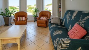 Una sala de estar con dos sillones de cuero, una mesa de centro de madera, un sofá verde con motivos de hojas y una estantería.