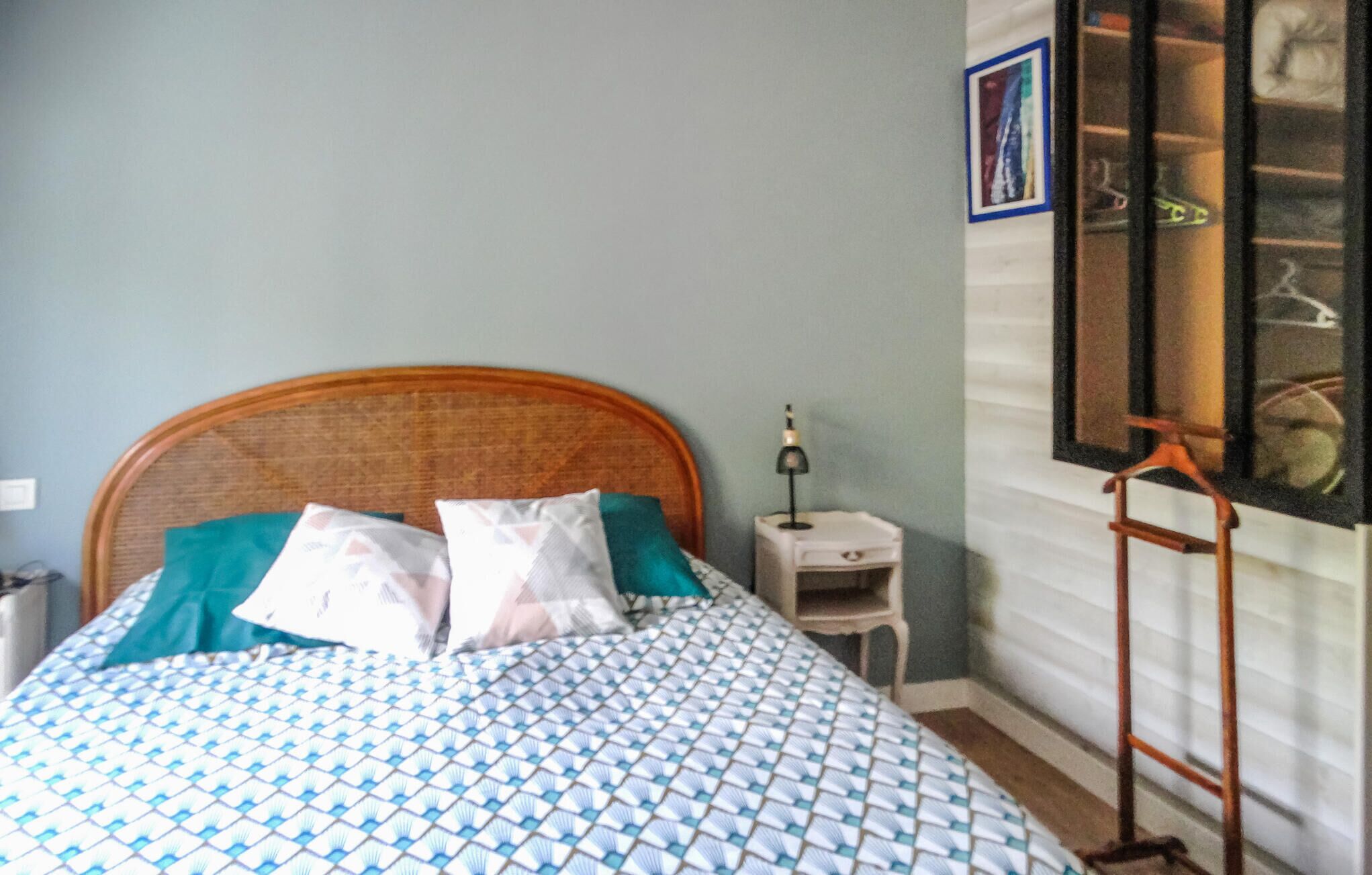A bedroom with a bed, pillows, a nightstand, a lamp, and a window with a view of the outside.
