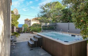Ein Whirlpool mit einer Holzterrasse und Stufen, umgeben von viel Grün und Blick aufs Meer.
