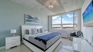 A modern bedroom with a large bed, a desk, and a view of the sky through a window. - Midtown Miami Marvel- Heated Pool & Prime Location (Miami)