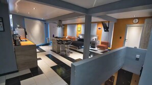 Un intérieur moderne comprenant une cuisine, un coin repas et un salon. Un escalier relie les différents niveaux.