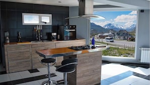 Une cuisine moderne dotée d’un îlot central, de tabourets de bar, d’une machine à café et offrant une vue sur un paysage montagneux enneigé.
