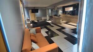 Un salon moderne avec un canapé, un sol à carreaux noir et blanc, un coin cuisine doté d’un bar et un téléviseur fixé au mur.