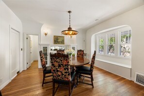 Ein Esszimmer mit Holztisch, floral gepolsterten Stühlen, einer Kandelaber und Blick durch große Fenster.