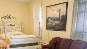 A bedroom with a bed, a rocking chair, a purple sofa, a patterned rug, and a painting on the wall. - Peaceful 1-bed studio cottage in Gering perfect for relaxing stay (Gering)
