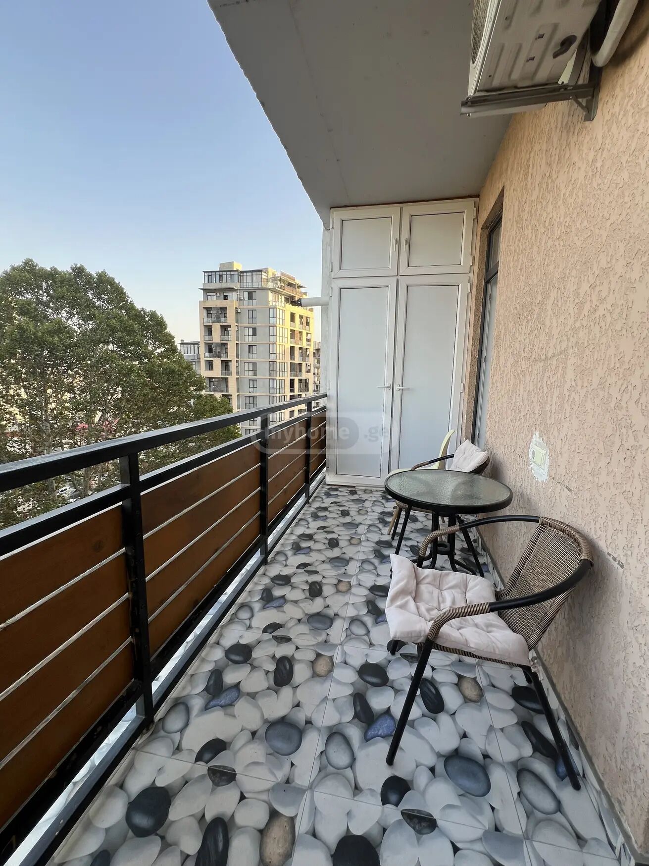 Un balcon avec un sol carrelé, une table avec des chaises et une porte.