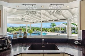 Eine Küche mit einem großen Fenster, das einen Pool und üppiges Grün zeigt.