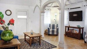Un salon avec une table basse en bois, un canapé bleu, un fauteuil à rayures, une bibliothèque et un téléviseur.