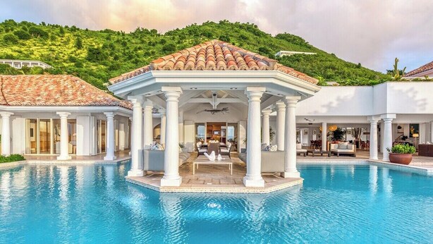 Un área de piscina con un pabellón, columnas blancas y vistas a una ladera verde exuberante.