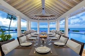 A covered dining area with a view of the ocean, white columns, and a central table set for a meal. - Petite Plage 5   Exclusive Beachfront Villa (Philipsburg)