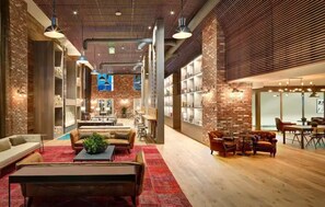 A spacious lobby with a red carpet, leather sofas, and a coffee table. There are bookshelves and a brick wall in the background. - 5-Star West Hollywood Living - Modern & Central (West Hollywood)