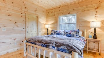 Une chambre à coucher située dans une cabane en bois, avec un lit, deux tables de chevet, une fenêtre et une porte.