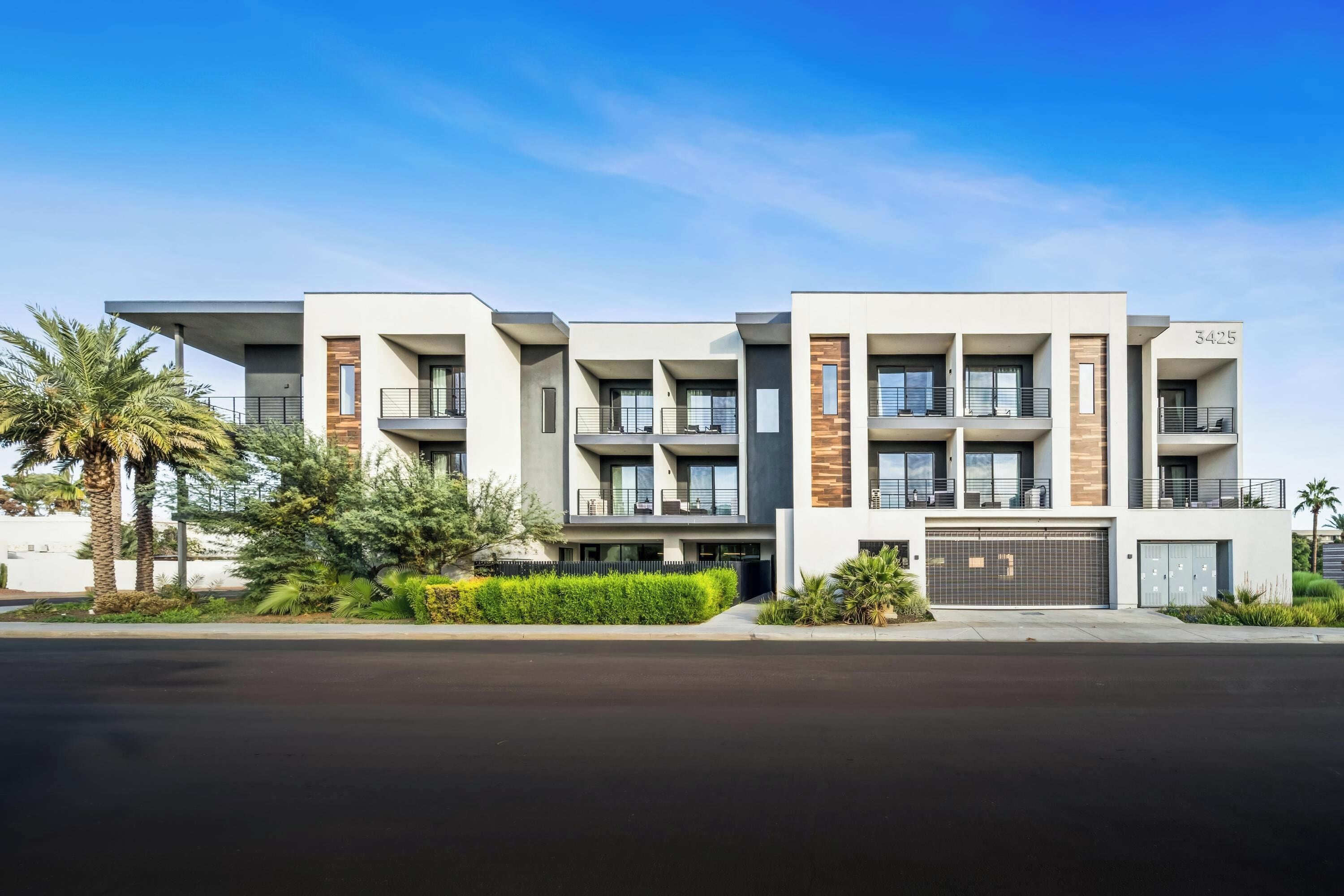 Un immeuble résidentiel moderne à plusieurs étages, doté de balcons, d’un garage et offrant une vue sur un ciel dégagé.