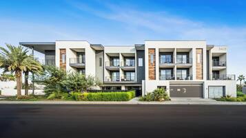 Un immeuble résidentiel moderne à plusieurs étages, doté de balcons, d’un garage et offrant une vue sur un ciel dégagé.