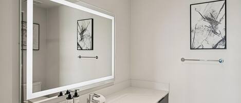Une salle de bain moderne avec un grand miroir, un lavabo et deux œuvres d’art encadrées accrochées au mur.