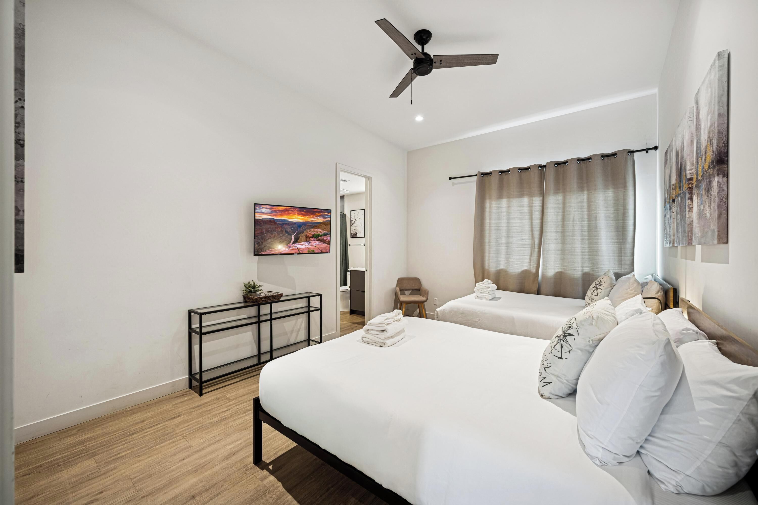Une chambre d’hôtel avec deux lits, un ventilateur de plafond, un tableau, une petite table et une vue sur l’extérieur.