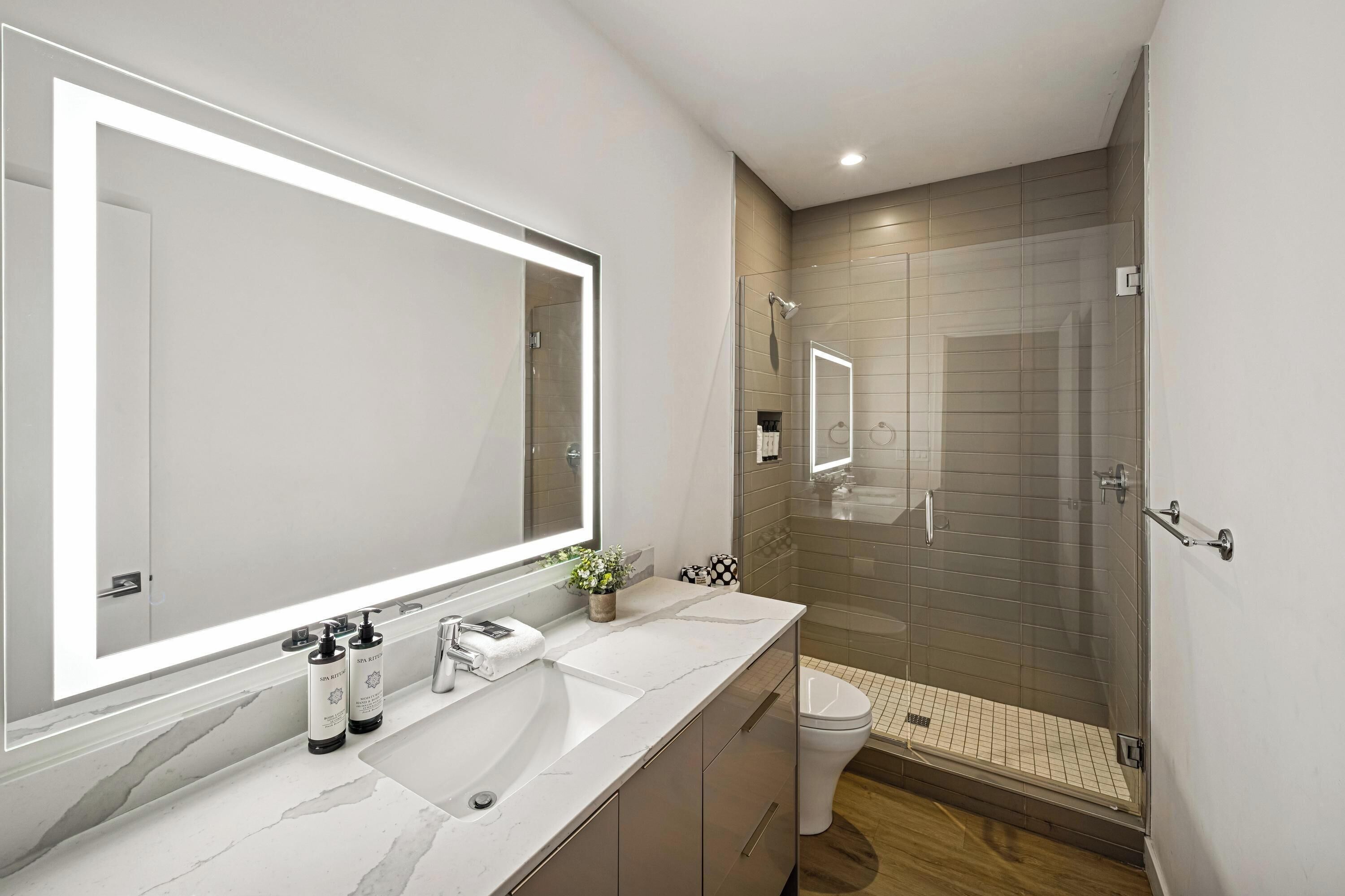 A modern bathroom with a large mirror, a sink, and a shower area.