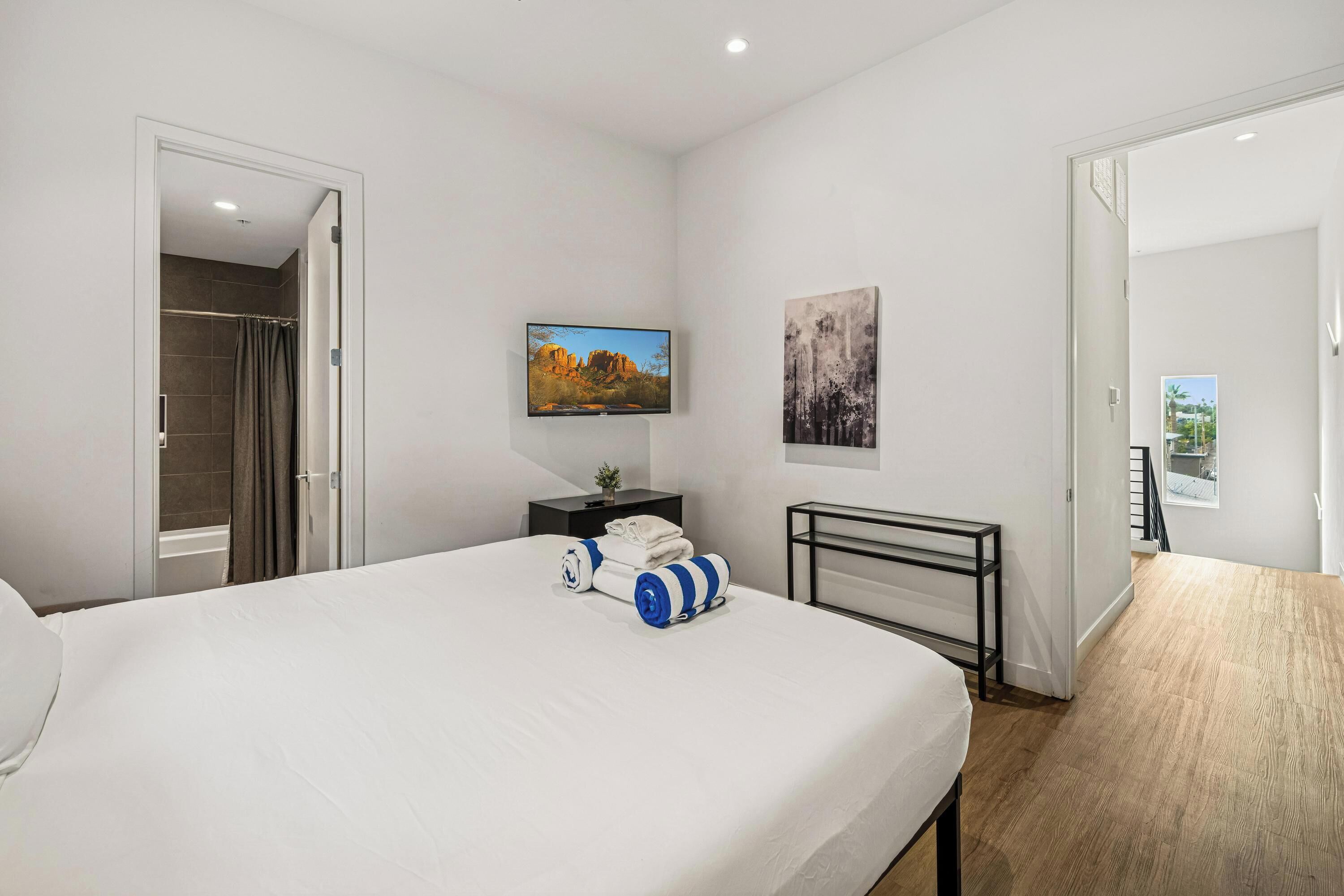 A modern hotel room with a large bed, a flat-screen TV, a painting, and a view of the outdoors.