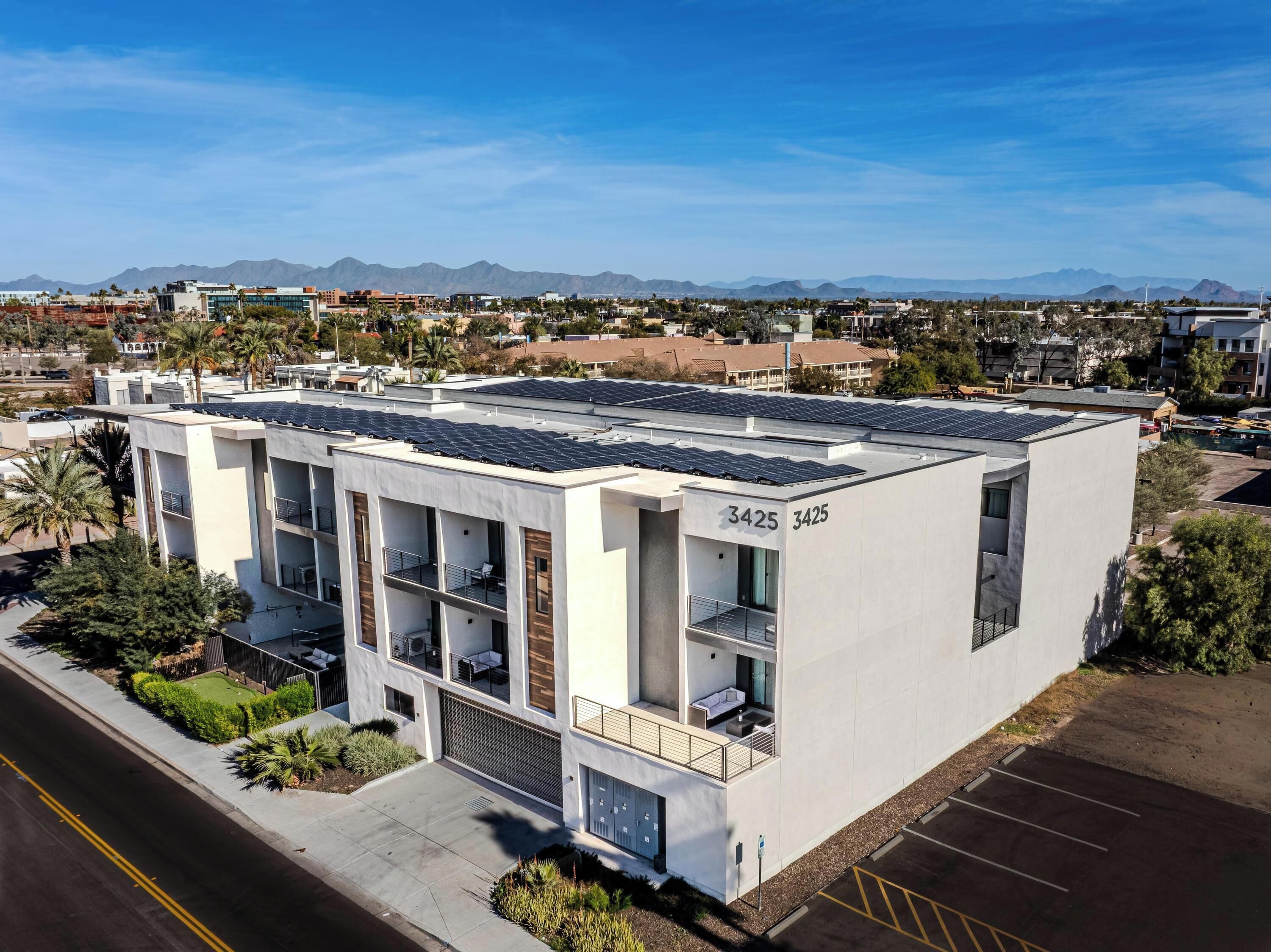 A modern building with solar panels on the roof, numbered 3425, featuring balconies and a parking lot.