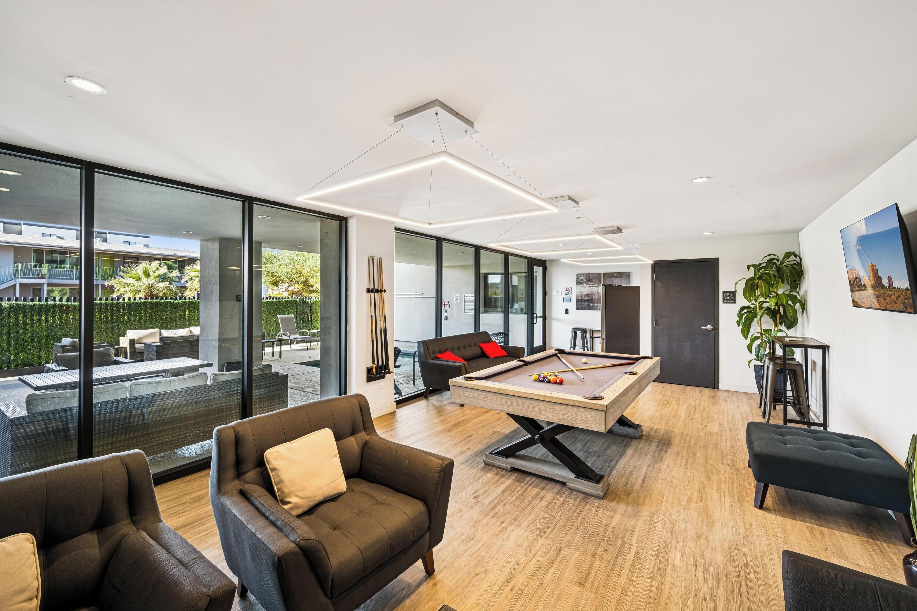 Un salon moderne doté d’une table de billard, de sièges confortables et de grandes fenêtres offrant une vue sur l’extérieur.