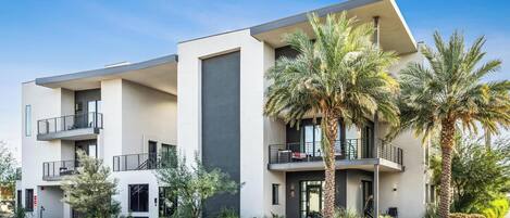 A modern multi-story building with balconies, palm trees, and a clear sky.