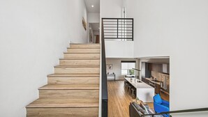 A modern staircase leading to a kitchen and dining area with wooden flooring and a blue sofa. - The Dune Lofts (Scottsdale)
