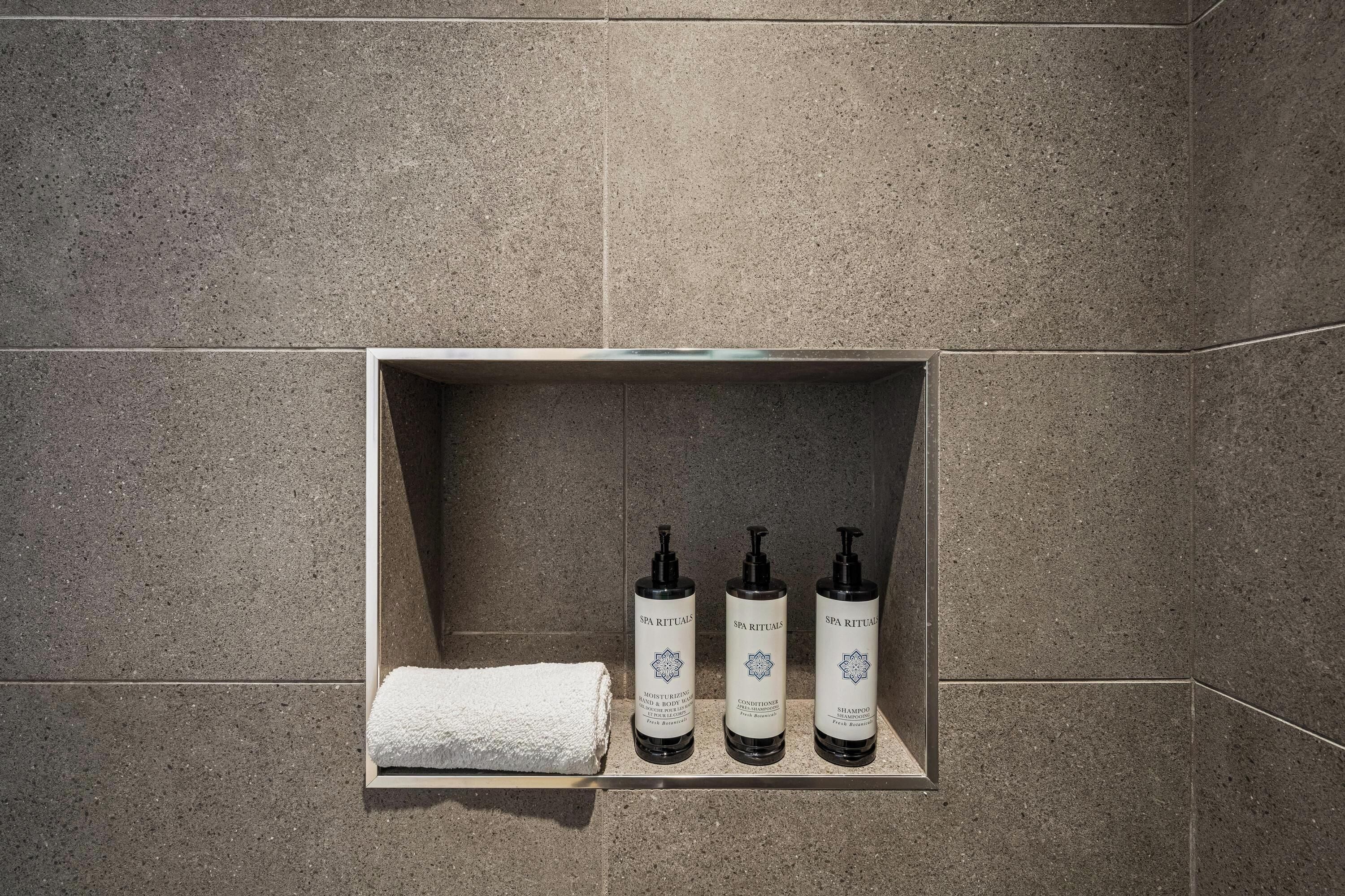 A bathroom with a shelf holding three bottles of SPA RITUALS body care products and a white towel.
