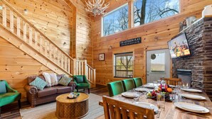 A wooden cabin interior with a dining area, a staircase, and a fireplace. - The Lookout Pair  (Sevierville)