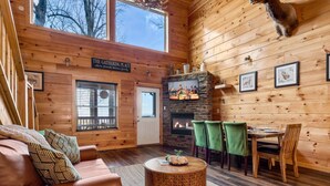 A cozy cabin interior with a fireplace, wooden walls, a dining area, and a sofa. - The Lookout Pair  (Sevierville)