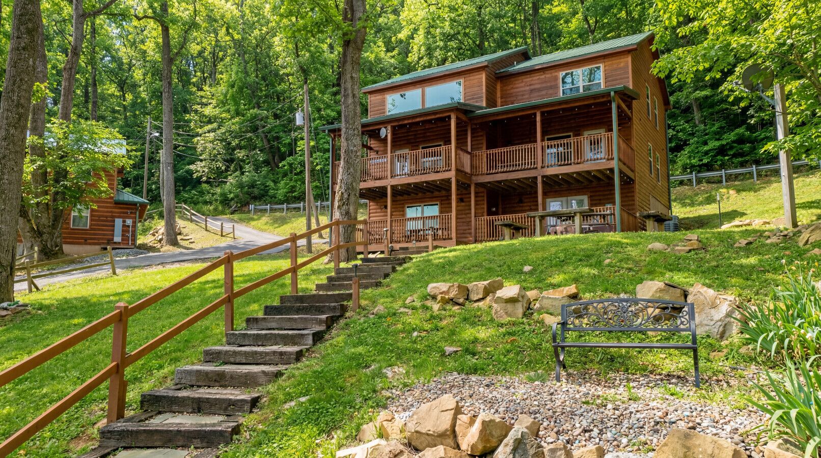 Une cabane en bois dotée d’un balcon, entourée d’arbres et accessible par un escalier en pierre.