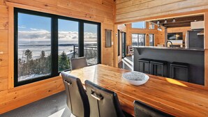 L’intérieur d’un chalet en bois comprend un coin repas, une cuisine et de grandes fenêtres donnant sur un paysage enneigé.