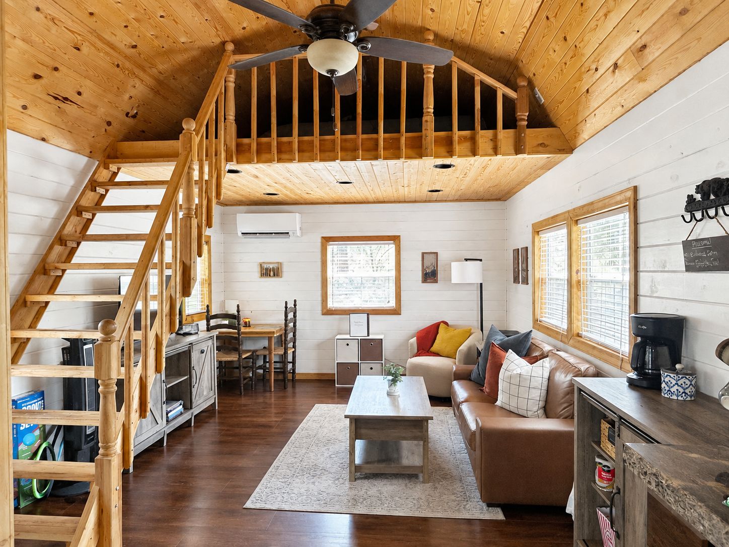 A spacious loft-style room with a wooden staircase, a dining area, a sofa, and a coffee station.