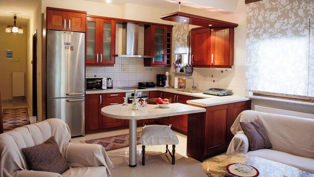 A modern kitchen with wooden cabinets, a stainless steel refrigerator, a dining table, and a sofa in the living area. - Anastasia s Kastoria Cozy Modern Garden Retreat (Kastoria)