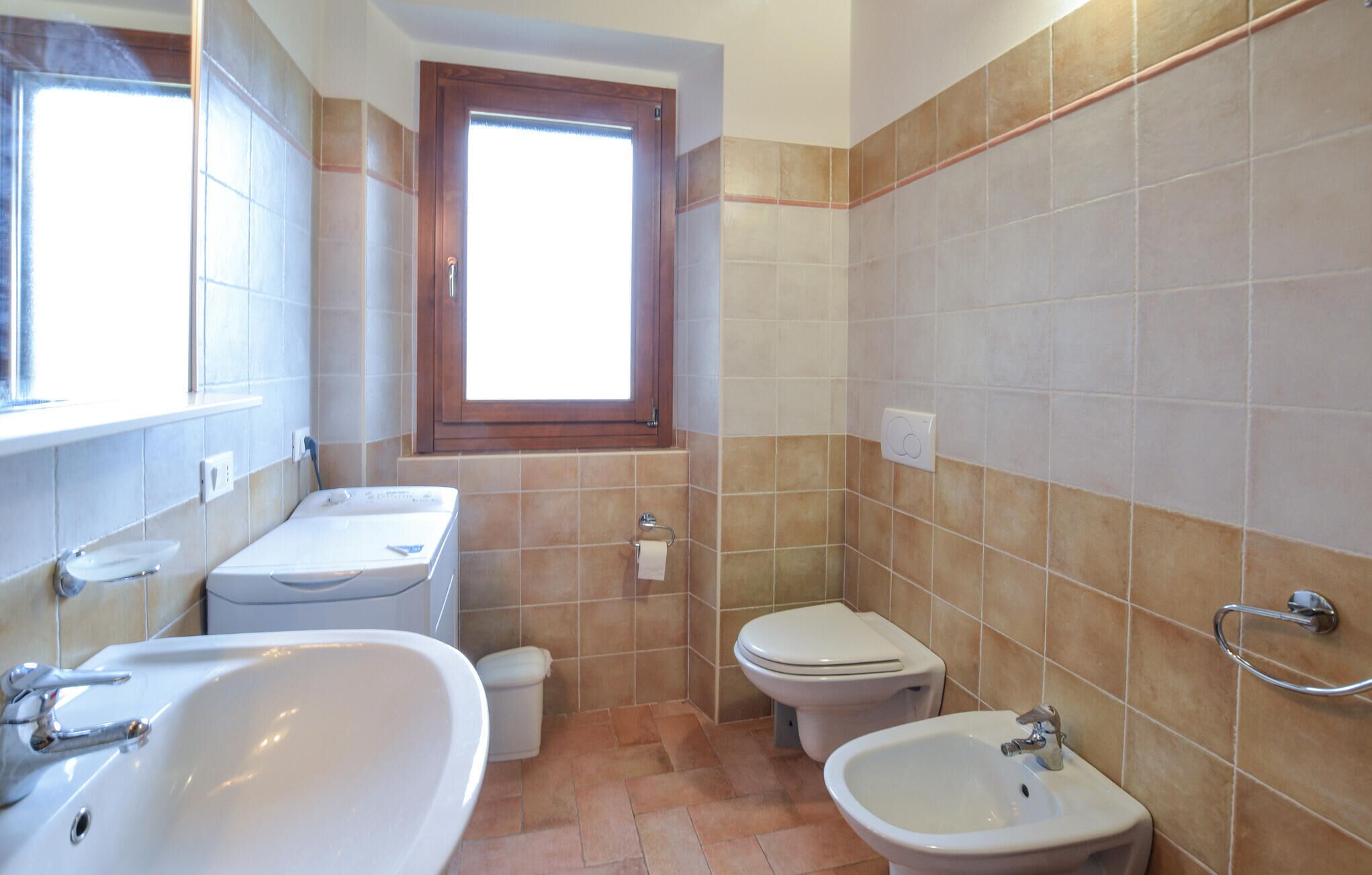 A bathroom with a sink, toilet, bidet, and a window.